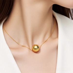 Detail of a minimalist gold sphere pendant necklace on a delicate metal chain
