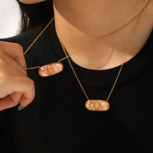 Detail of gold oval pendant with shell motif and colorful resin inlay on a necklace