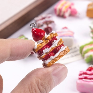 Handheld view of a detailed miniature strawberry napoleon cake resin pendant for DIY crafts