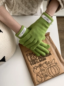 Detail of grass green knitted gloves with a retro white woven label on the wrist
