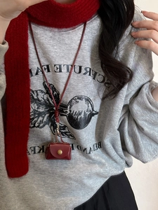 Detail of red leather mini neck pouch with gold snap and woven cord worn on a hoodie