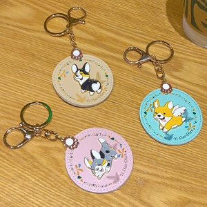 Three cute cartoon Corgi leather keychains in beige, blue, and pink on a wooden surface