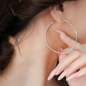 Macro view of textured silver metal hoop earring worn on a model with a warm skin tone