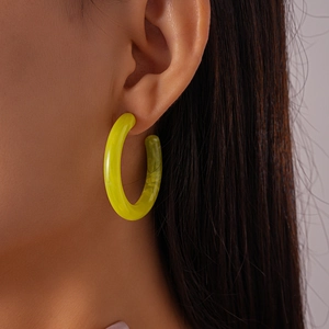 Close-up of a model wearing a thick yellow resin hoop earring with a glossy finish