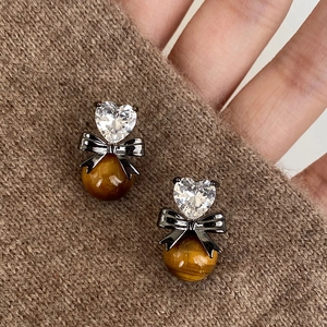 Macro shot of tiger eye stone heart earrings with black bows on a brown sweater background