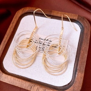 Macro shot of gold and silver layered circular fringe earrings on a wooden display tray