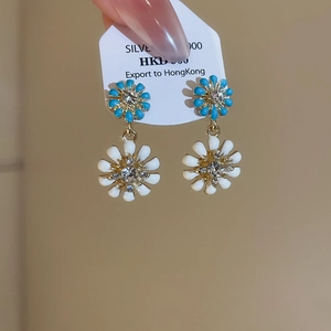 Detailed close-up of blue and white enamel daisy earrings with sparkling rhinestones