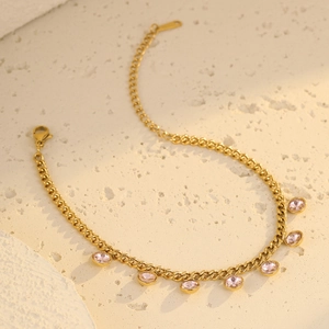 Close-up of golden chain bracelet with pink round gemstone charms on beige background