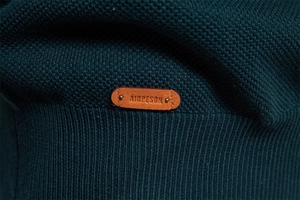 Detail der Strickstruktur mit Leder-Markenetikett und Metallniete auf tiefblauem Gewebe