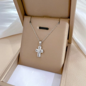 Detailed close-up of a silver titanium cross pendant with sparkling zircon in a beige jewelry box
