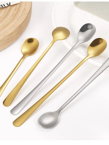 Polished stainless steel round spoons in gold and silver finish on a wooden board