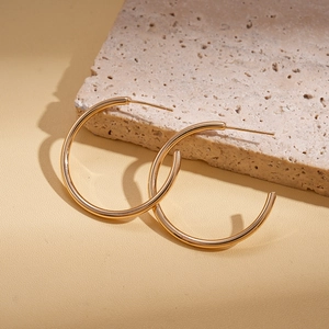 Detail of minimalist gold round hoop earrings on a textured stone surface
