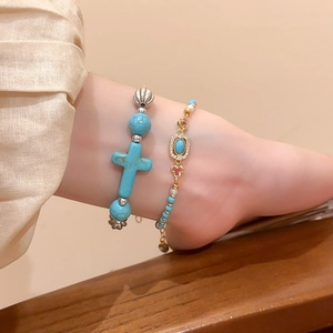 Detail of beaded turquoise cross bracelet and gold chain jewelry on a model's wrist