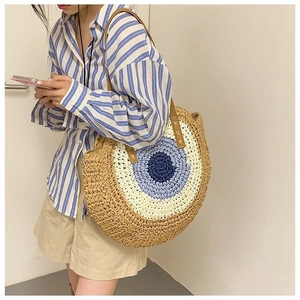 Detail of handwoven round straw beach bag with an evil eye pattern and leather handles