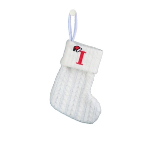 Close-up of white knitted Christmas stocking with red embroidered letter I and Santa hat