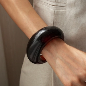 Detail of chunky amber resin open bangle on model showing translucent glossy finish