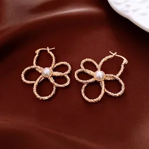 Elegant gold flower hollow earrings with central pearl on dark velvet background