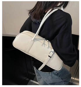 Close-up of a white baguette shoulder bag on model showing strap and metal buckle detail