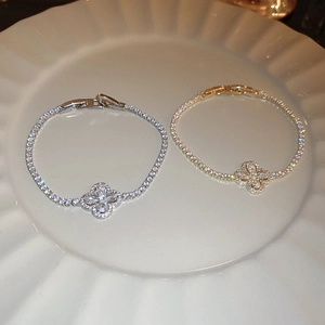 Détail de bracelets trèfle en zircon doré et argenté sur une assiette en céramique blanche