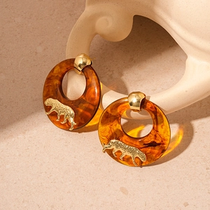 Macro detail of amber resin earrings featuring a golden tiger head and metal clasp