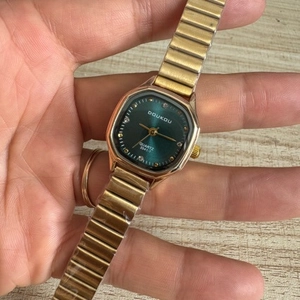 Minimalist square green dial watch with gold elastic strap shown on a woman's wrist