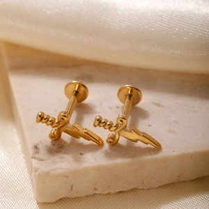 Golden stainless steel dagger stud earrings displayed on marble and silk fabric