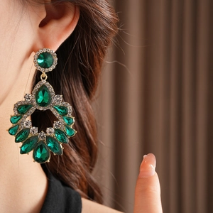 Gros plan de boucles d'oreilles dorées avec gouttes vertes portées par un mannequin