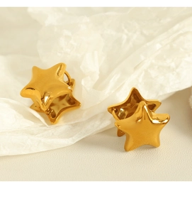 Macro shot of minimalist gold star-shaped stud earrings on a textured white surface