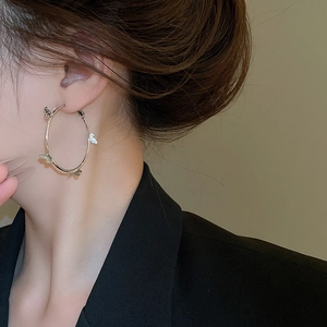 Detail shot of a large silver hoop earring with small butterfly charms worn by a model