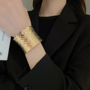 Close-up of golden wide cuff bracelet with woven texture on model's wrist with black suit