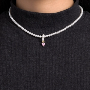 Detail view of pearl necklace with a pink heart pendant and green leaf on a model