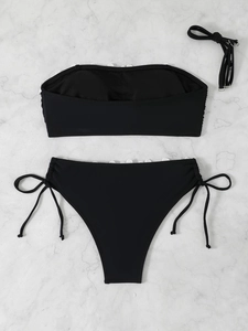 Flat lay of black two-piece bikini with white lace trim and side-tie detailing