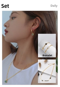 Detail of gold titanium steel jewelry set with heart charms and green stone earrings
