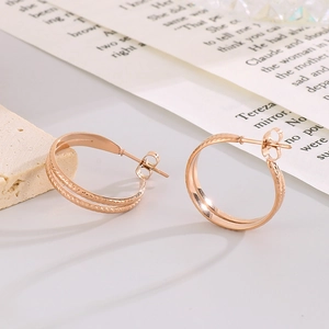 Rose gold double hoop earrings with textured wheat design on a minimalist background