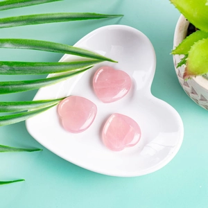 Three polished natural pink rose quartz heart stones in a white ceramic dish detail