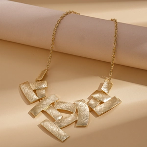Detail of gold geometric necklace with textured brushed metal finish on diagonal props