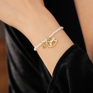 Detailed view of pearl bracelet with gold rocking horse charm on a model's wrist