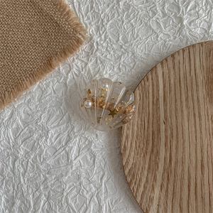 Macro detail of transparent shell hair clip with gold foil and pearls on wooden base