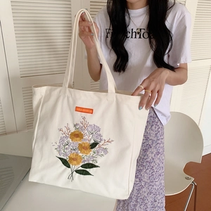 Close-up of intricate sunflower embroidery on white canvas tote bag with orange tag