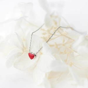 Elegant red heart pendant necklace with silver chain on white petals background