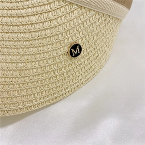 Detail shot of beige straw sun hat featuring a premium gold M-letter metal badge decoration