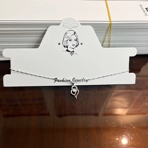 Detailed view of silver necklace with double-heart pendant and clear gemstone on a display card