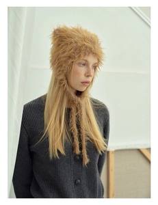 Detail of fluffy faux fur earflap hat with long braided tassels in light golden brown
