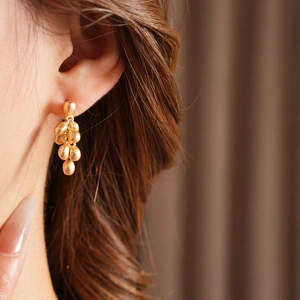 Close-up of golden bean cluster drop earrings with a textured matte metallic finish