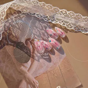 Detail of pink gradient press-on nails with floral patterns and rhinestones on lace