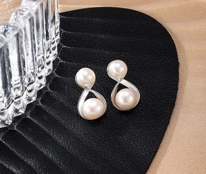 Detail view of cross S925 silver stud earrings with two white pearls on black leather