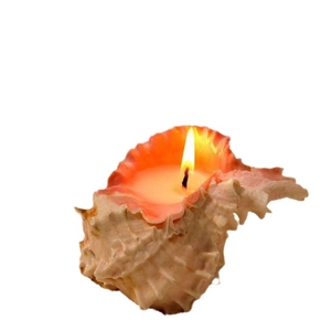 Handmade shell scented candle with orange rim and lit flame on white background