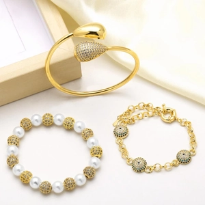 Three-piece gold jewelry set with pearl bracelet, teardrop bangle and evil eye charms