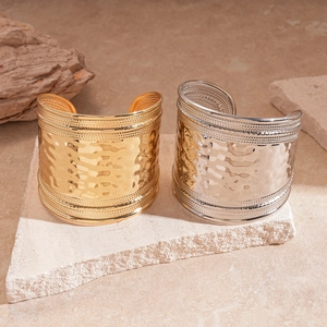 Hammered gold and silver wide bangles with beaded borders on a neutral stone display