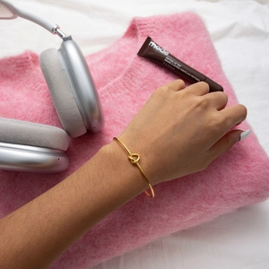 Detail of 18K gold stainless steel knotted bangle worn with trendy lifestyle accessories